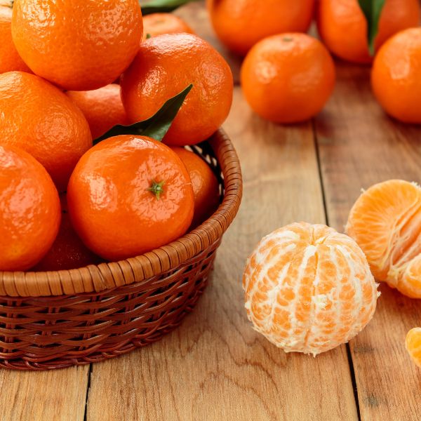Peeled clementines on a table next to a basket full of them